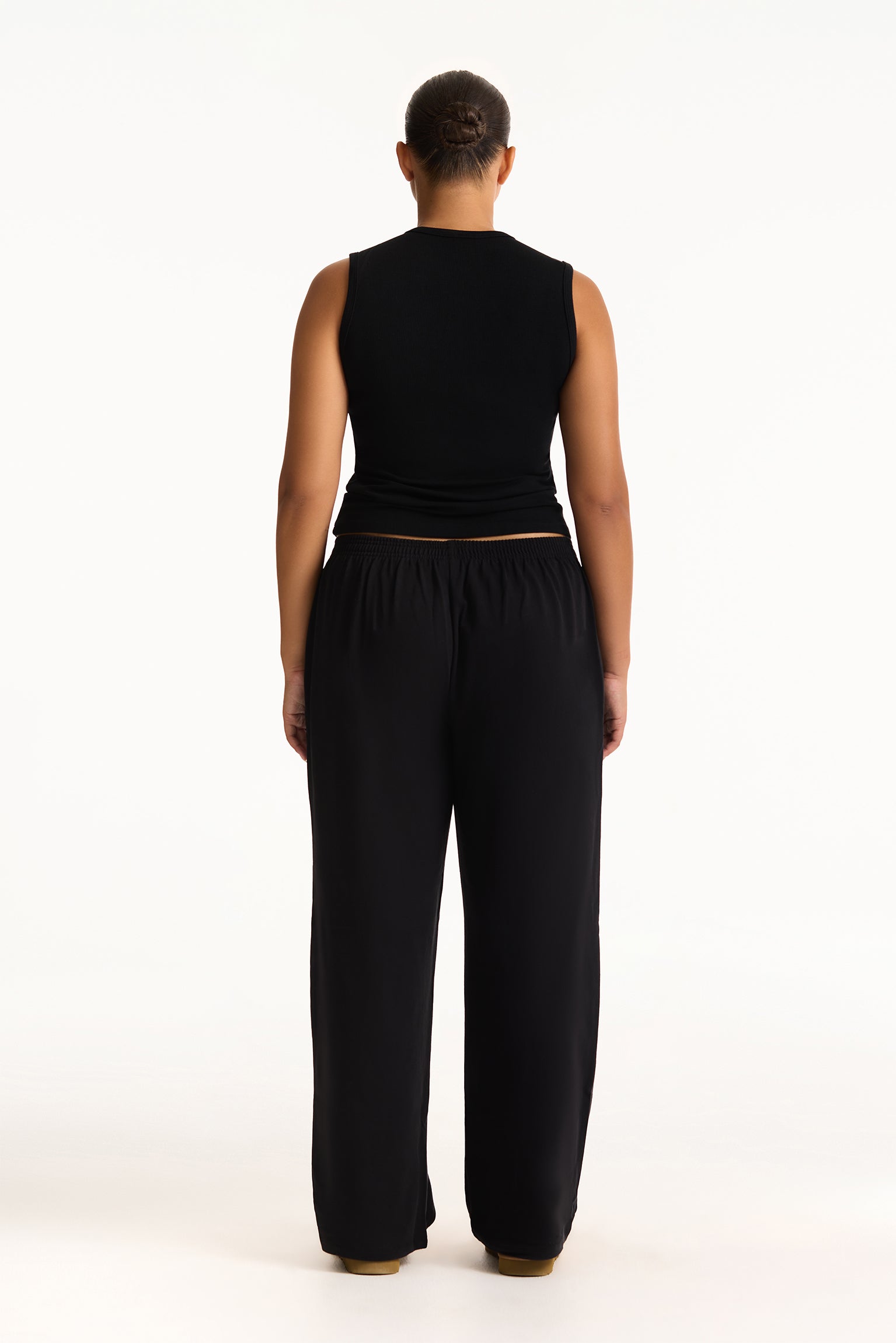 Person wearing a black sleeveless top and black pants on a white background