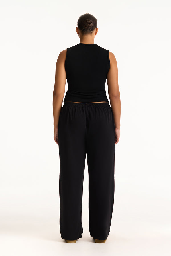 Person wearing a black sleeveless top and black pants on a white background