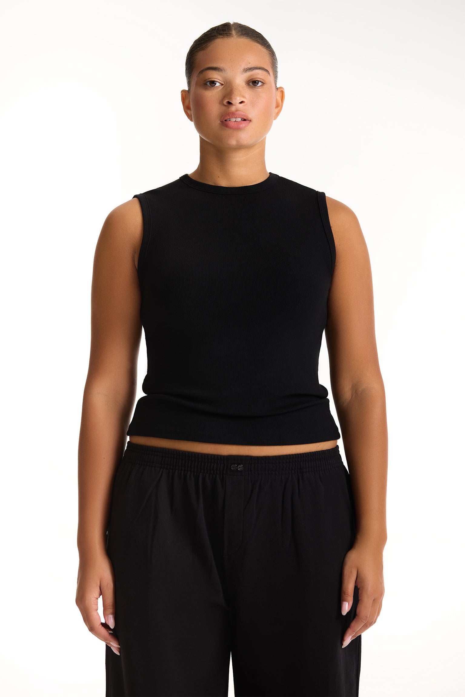 Woman wearing a black sleeveless top and black pants on a white background <model-info>Jade wears a size L and is 5’9”, 30” waist, 38” bust.</model-info>
