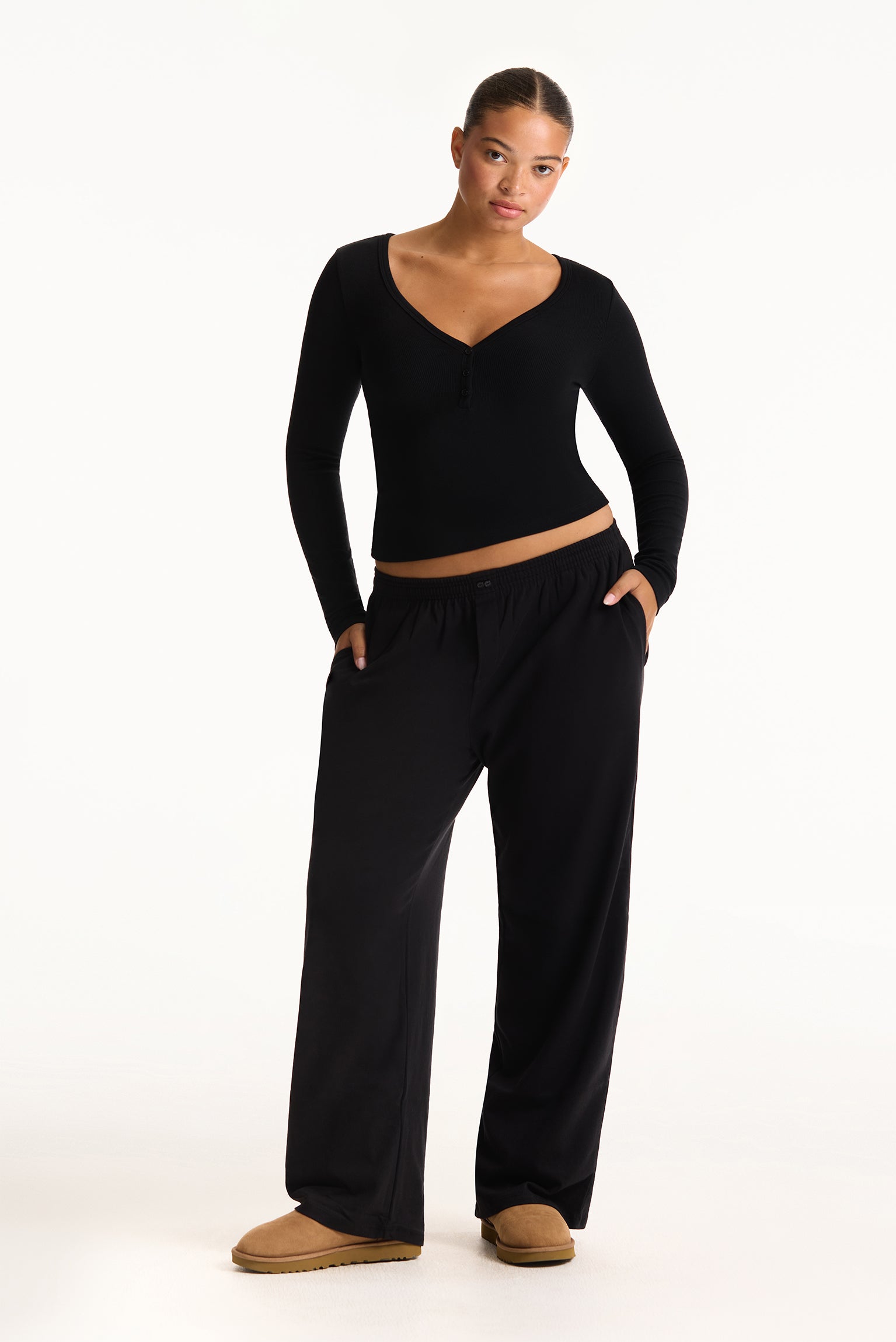 Woman wearing a black long-sleeve top and black wide-leg pants on a white background