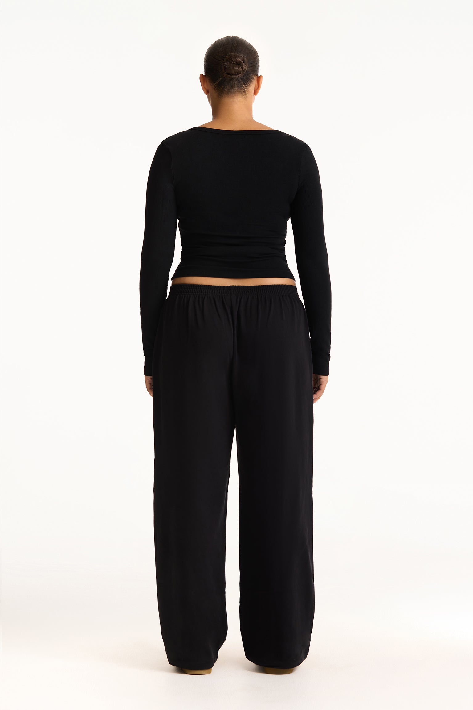 Person wearing a black long-sleeve top and black wide-leg pants on a white background
