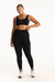 Woman wearing a black sports bra and leggings with white accents on a white background