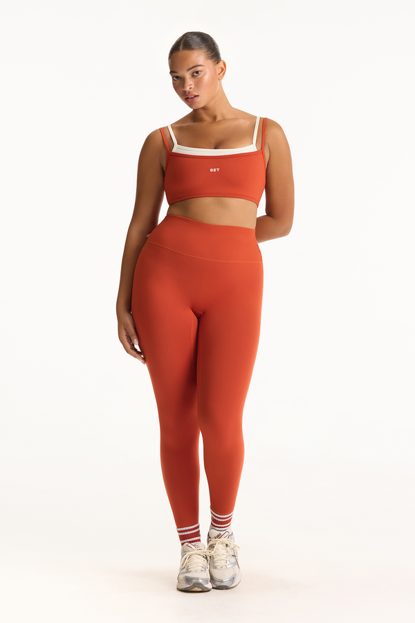 Woman wearing an orange sports bra and leggings set on a white background