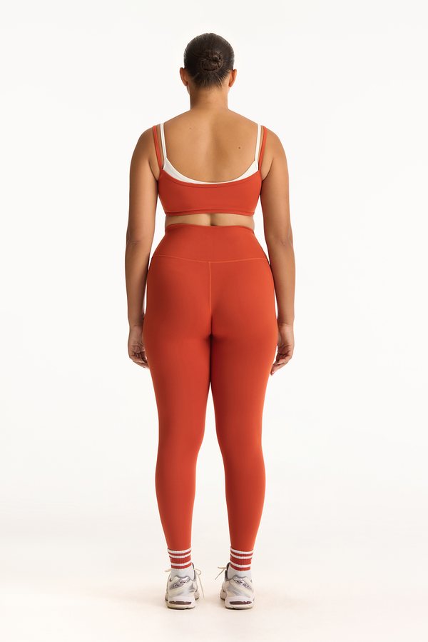 Person wearing an orange sports bra and leggings set on a white background