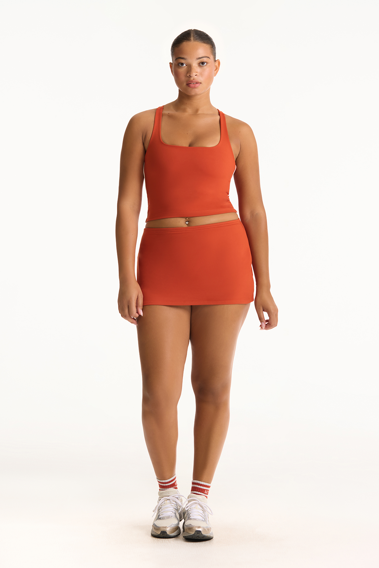 Woman wearing an orange tank top and skirt set on a white background