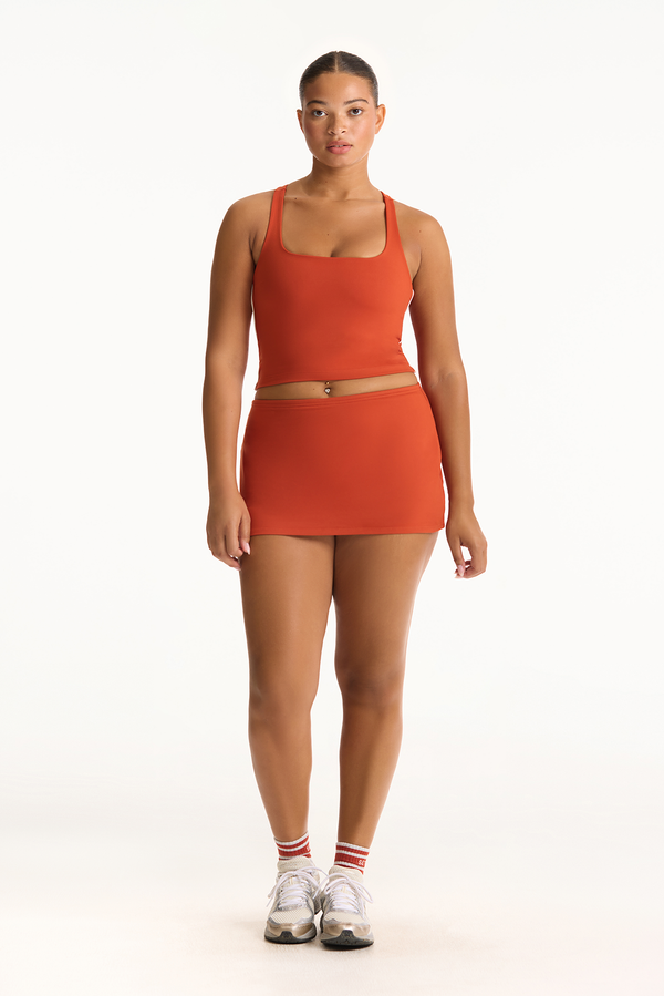 Woman wearing an orange tank top and skirt set on a white background