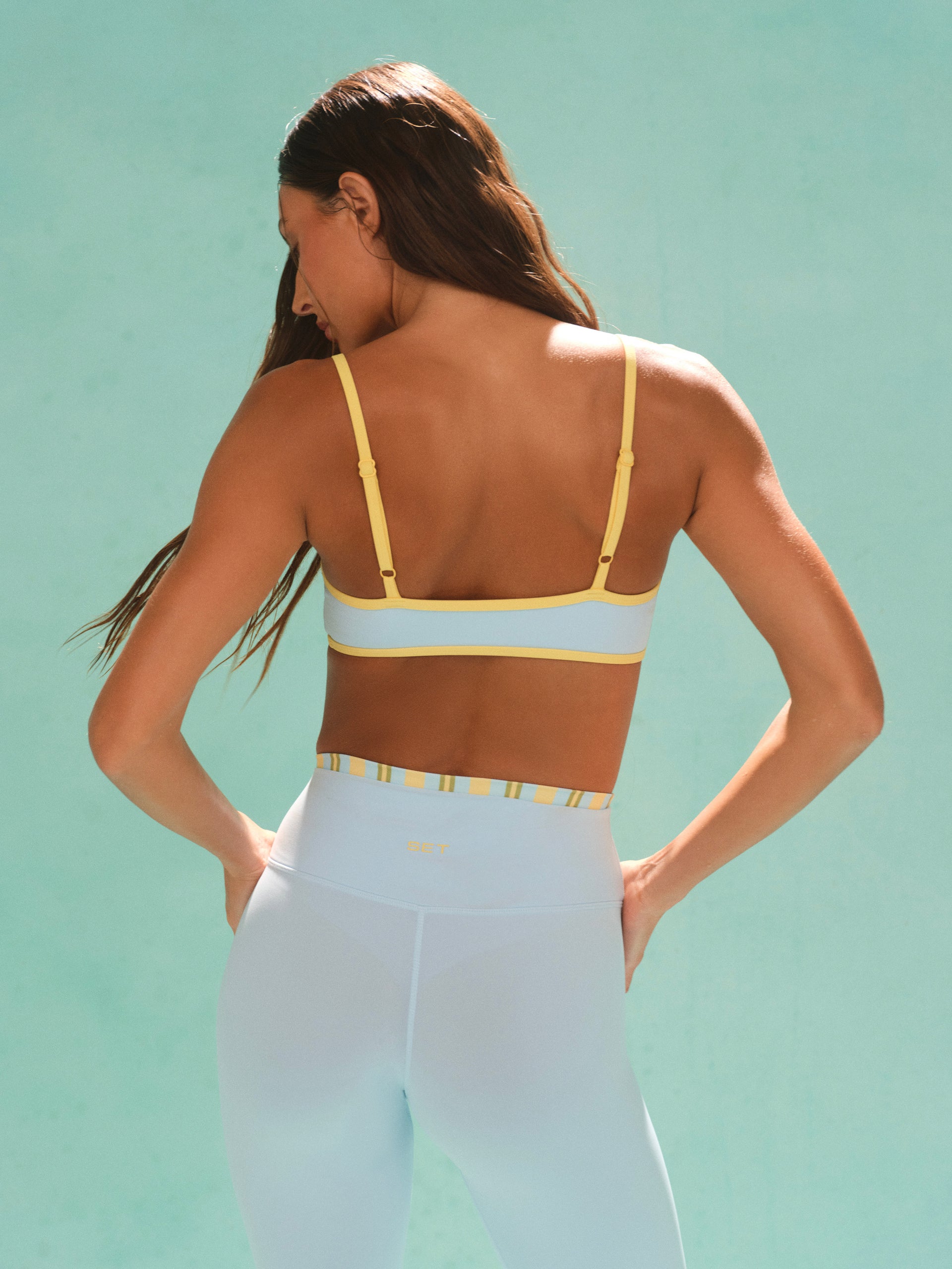 Woman wearing a yellow sports bra and white leggings against a light blue background
