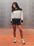A woman modeling a white, black, and navy striped long-sleeve crewneck sweatshirt with matching black athletic shorts, white socks, and white sneakers, standing on a terracotta-colored surface against a textured gray background. <model-info>Alana wears a size M and is 5’8”, 28” waist, 35" bust.</model-info>