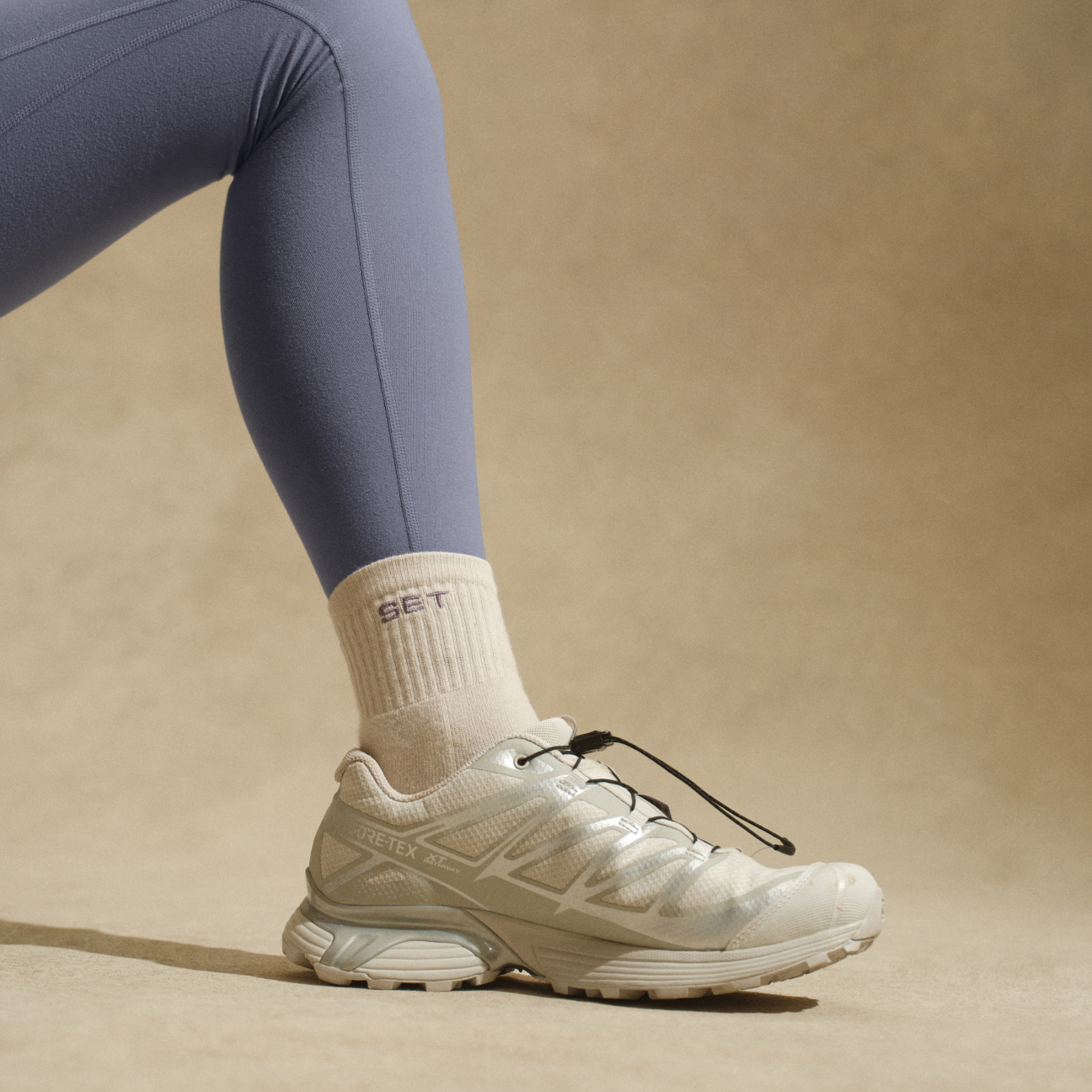 Bent leg featuring a purple legging, sock and shoe on neutral background