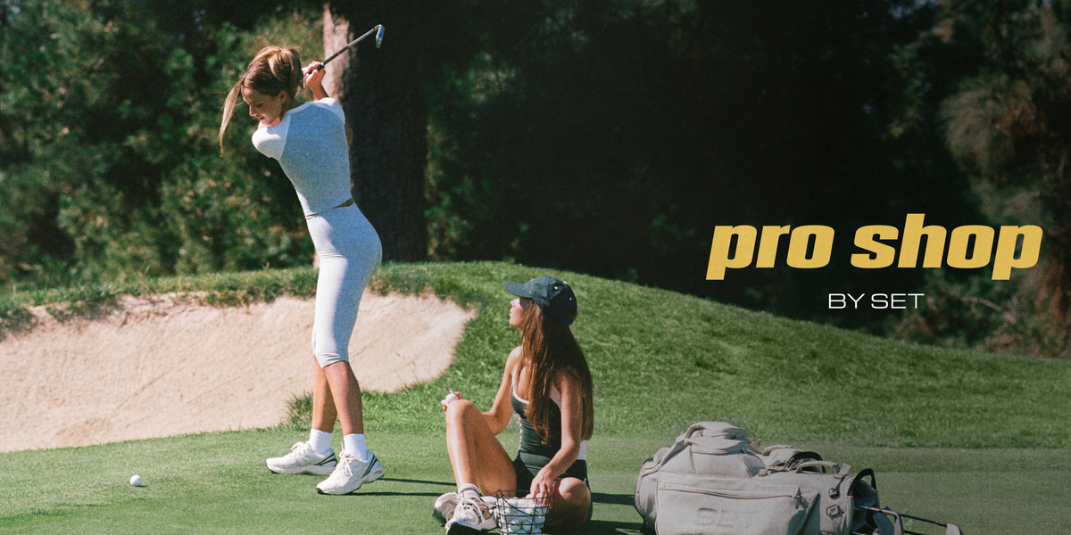 A lifestyle shot on a golf course featuring a woman in a white athletic set mid-swing, another woman sitting nearby, and a golf bag on the grass, with 'pro shop BY SET' text overlay on the right.