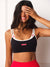 A woman wearing a black sports bra with white trim and small red accents, paired with bright red leggings, posing against a white wall. <model-info>Meeya wears a size XS and is 5’8”, 23” waist, 32B bust.</model-info>