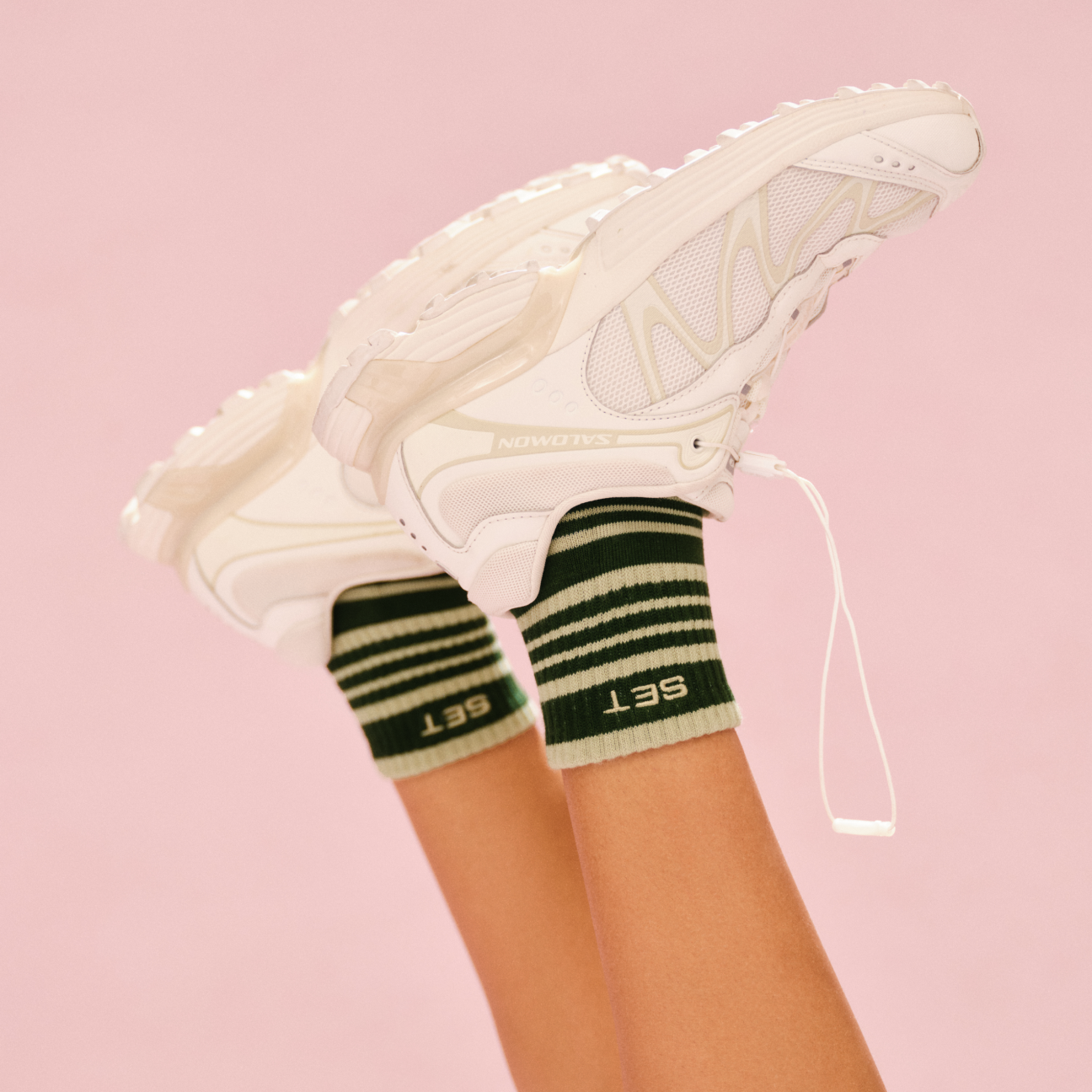 White sneakers with green striped socks on a pink background