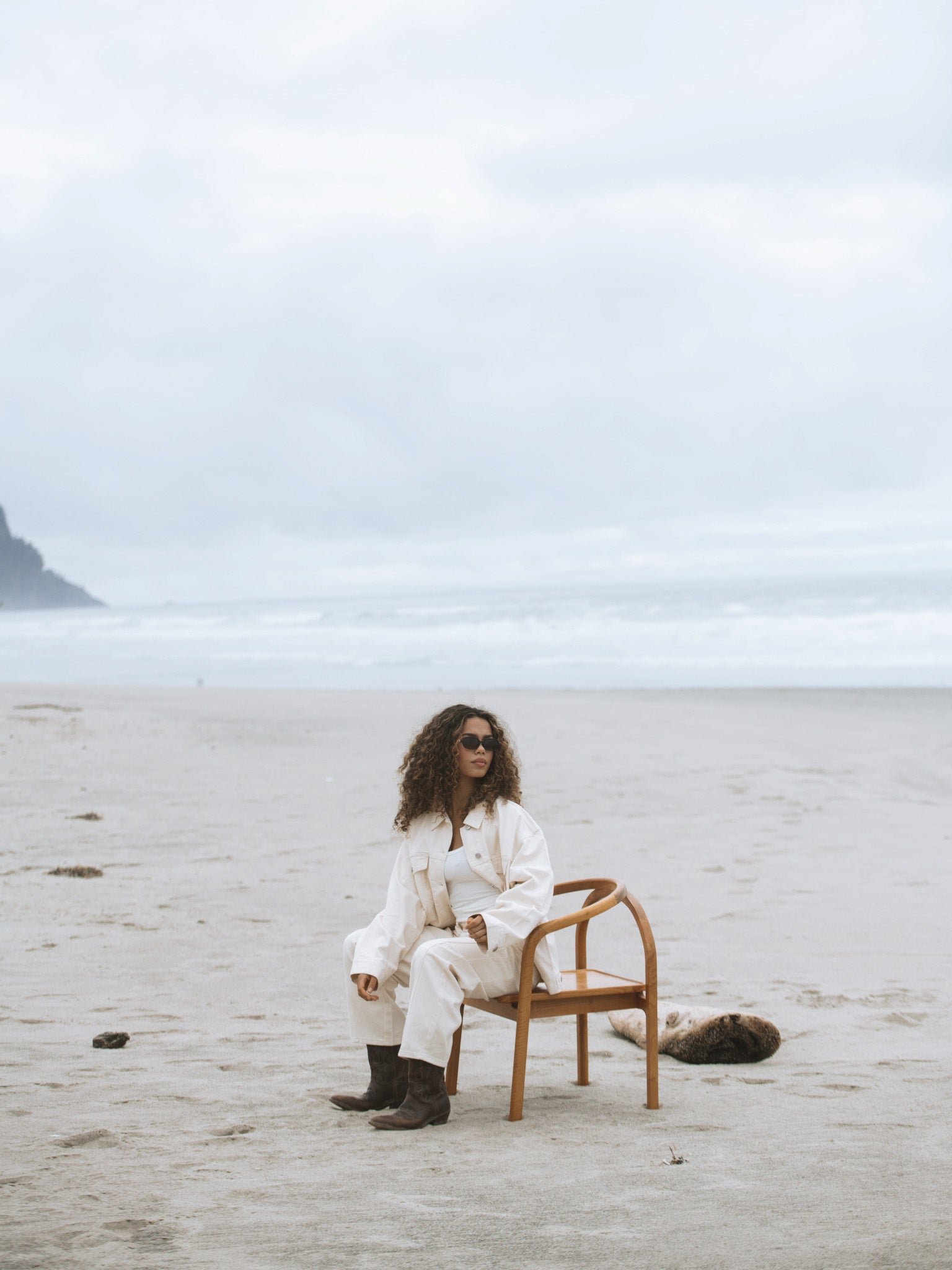 Girl wears cream outfit while sitting on a chair on the beach