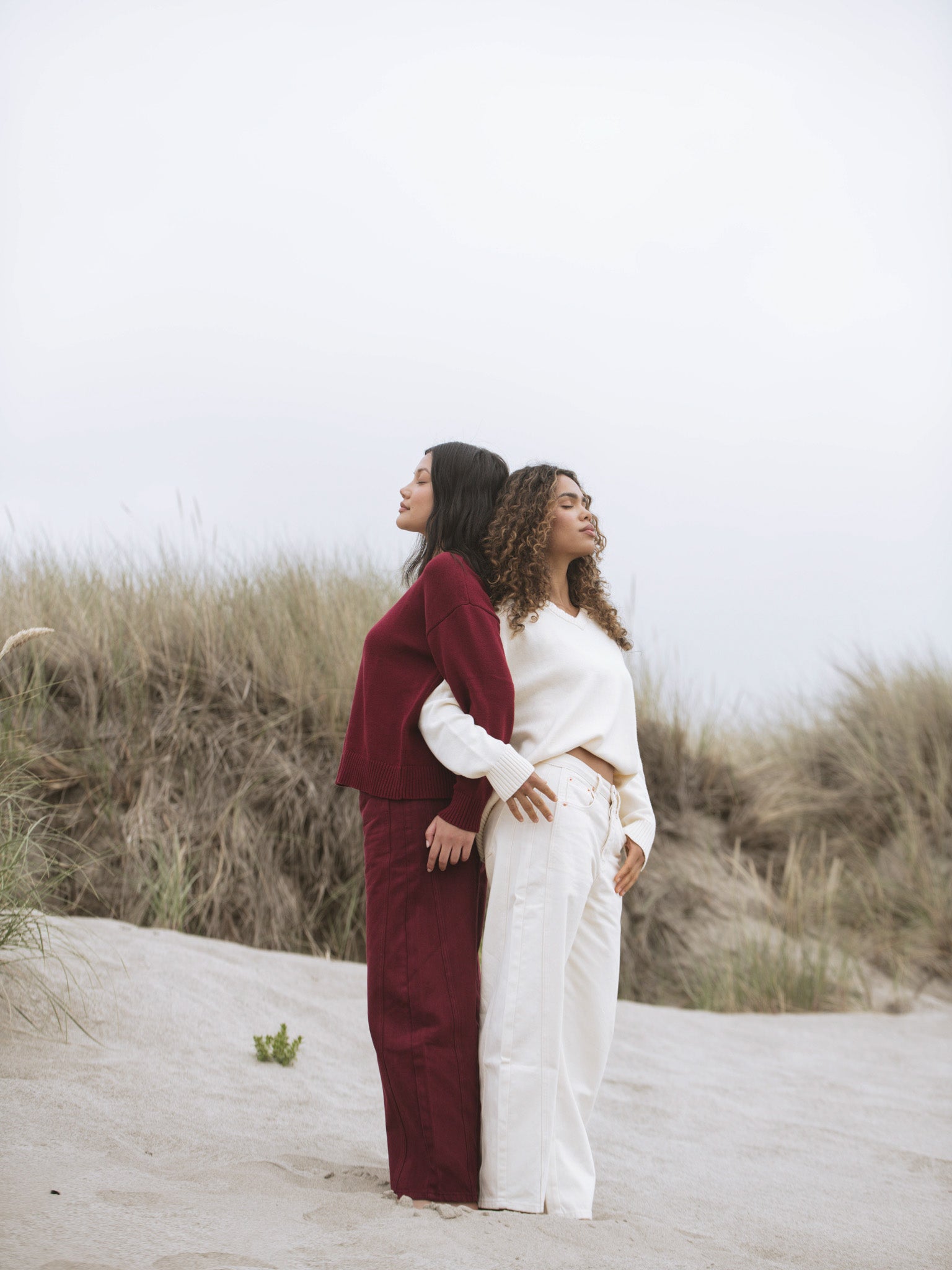 Two women standing on a sandy path with grasses in the background