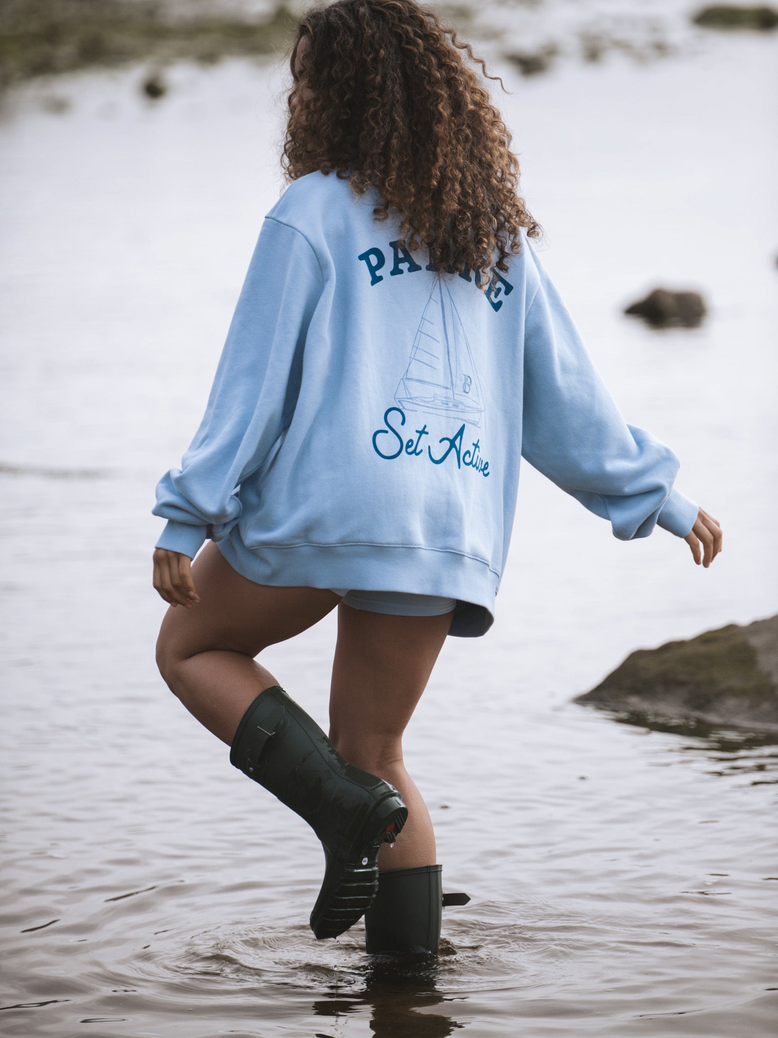 Person wearing a light blue sweatshirt with text, standing in water.