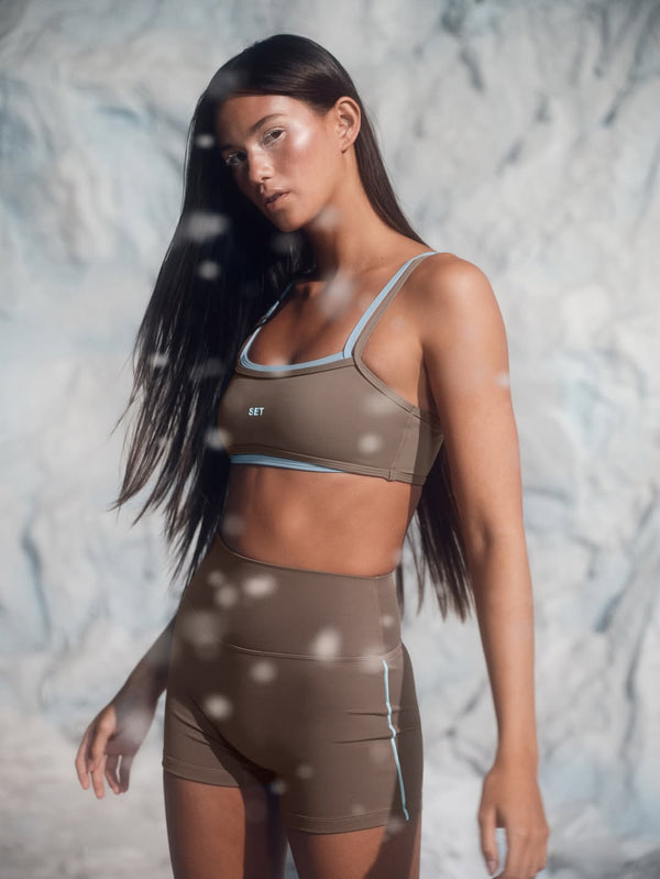 Woman wearing a brown sports bra and shorts set against a marble background