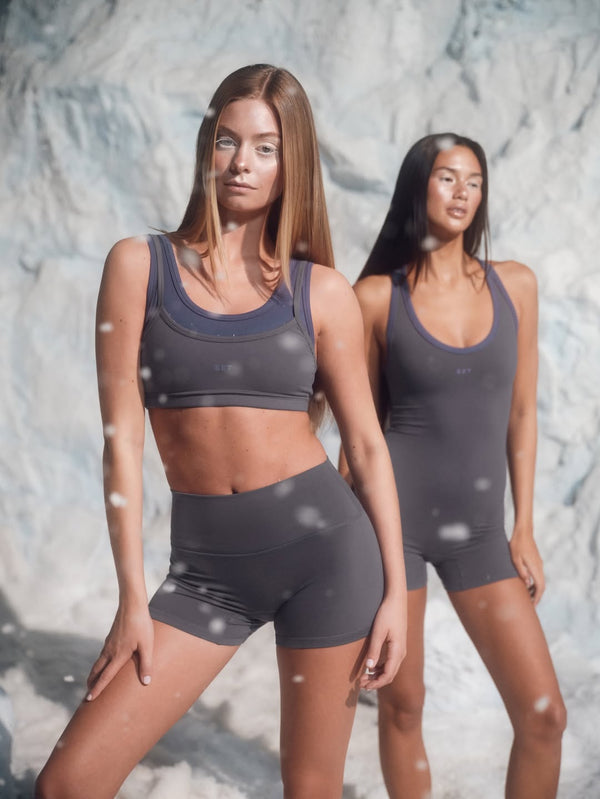 Two women wearing matching gray athletic outfits against a textured wall.