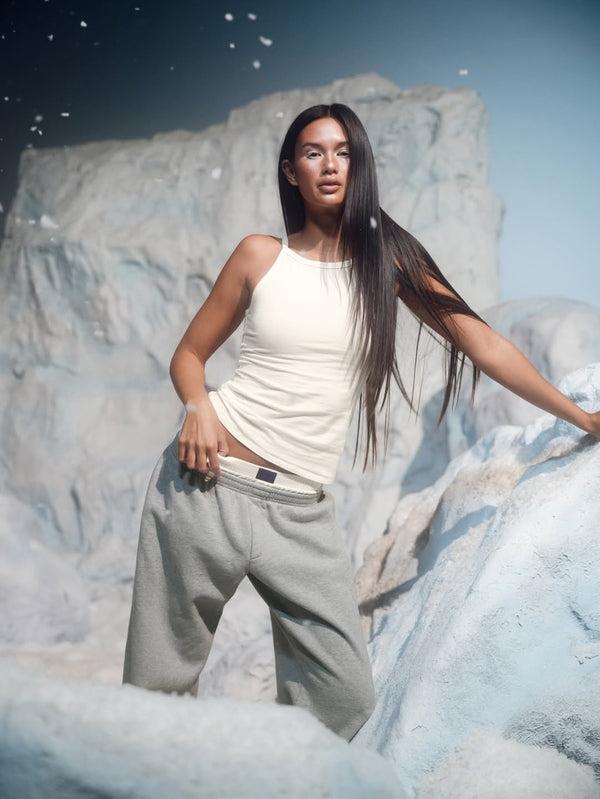 Woman in a white top and light gray pants standing on a snowy landscape.