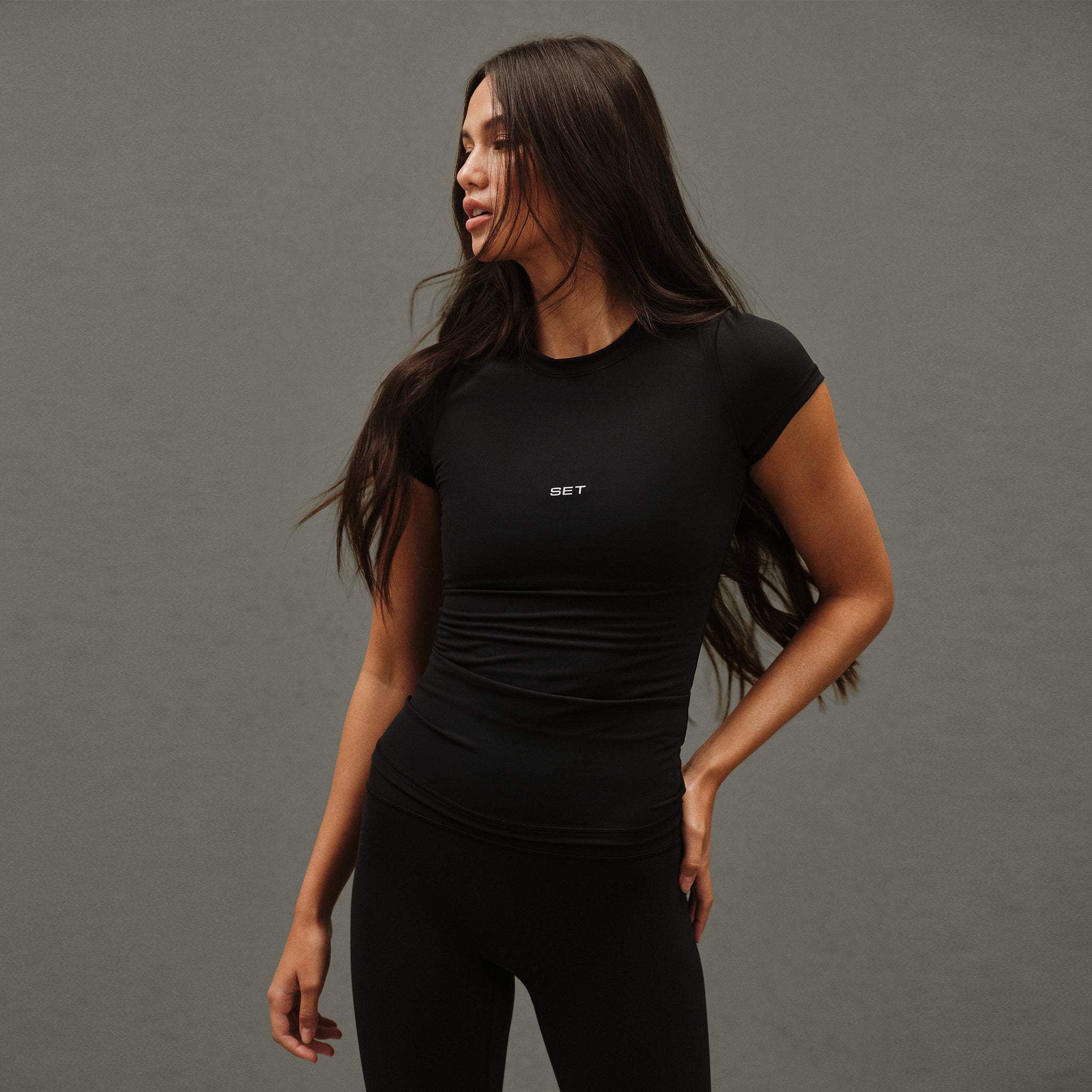 Woman wearing a black athletic outfit with a brand logo on a gray background