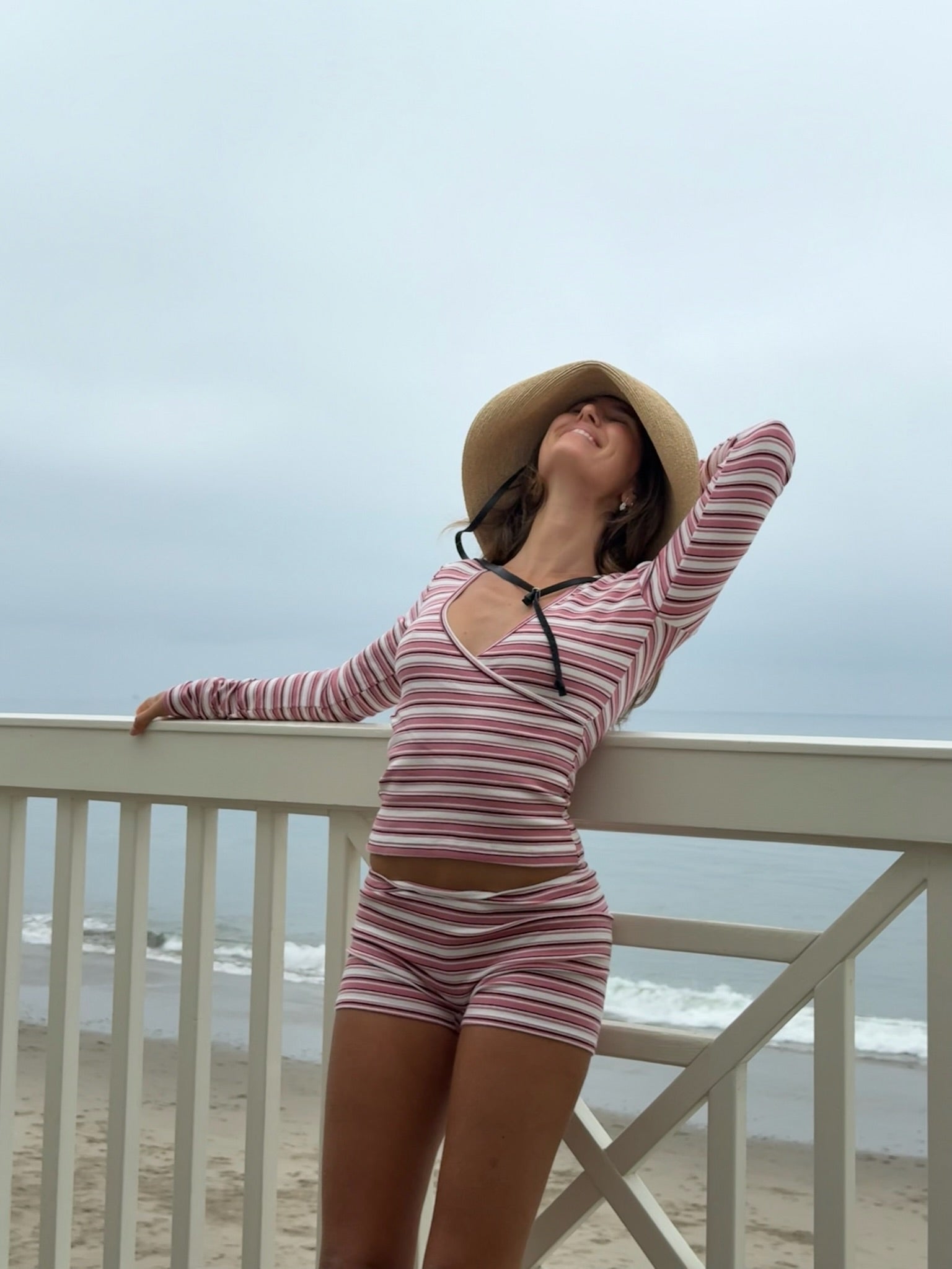 Woman in a striped set and sun hat standing on a beach deck with ocean view.
