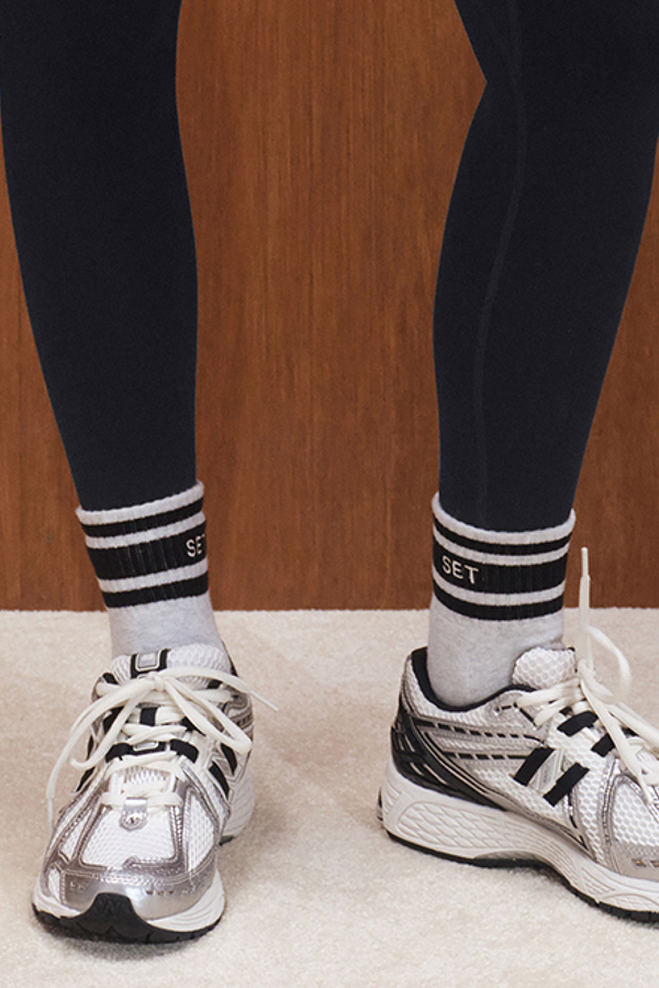 Person wearing black leggings, white socks with black stripes, and silver athletic shoes on a wooden floor.