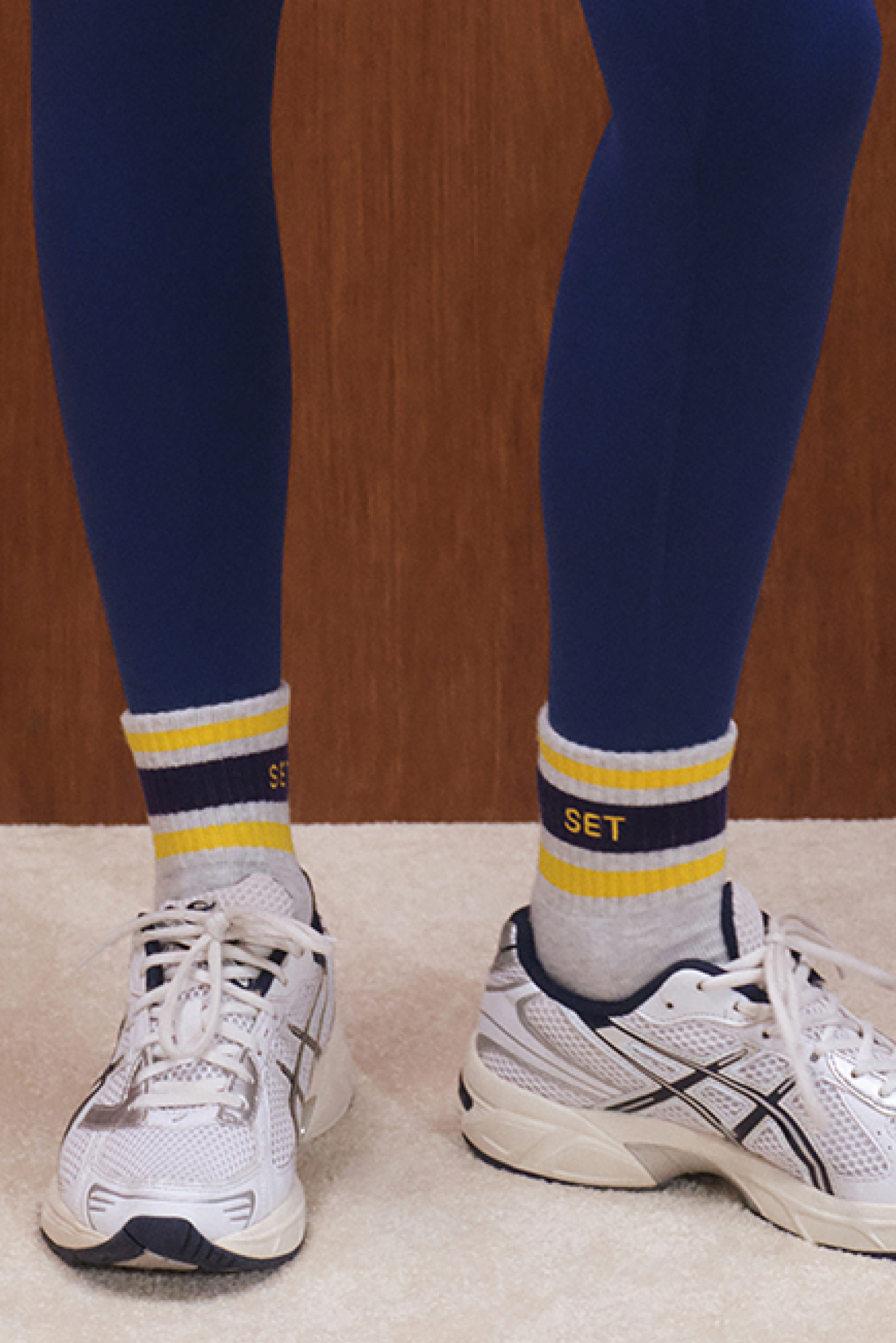 Person wearing blue leggings and white sneakers with yellow and navy striped socks.