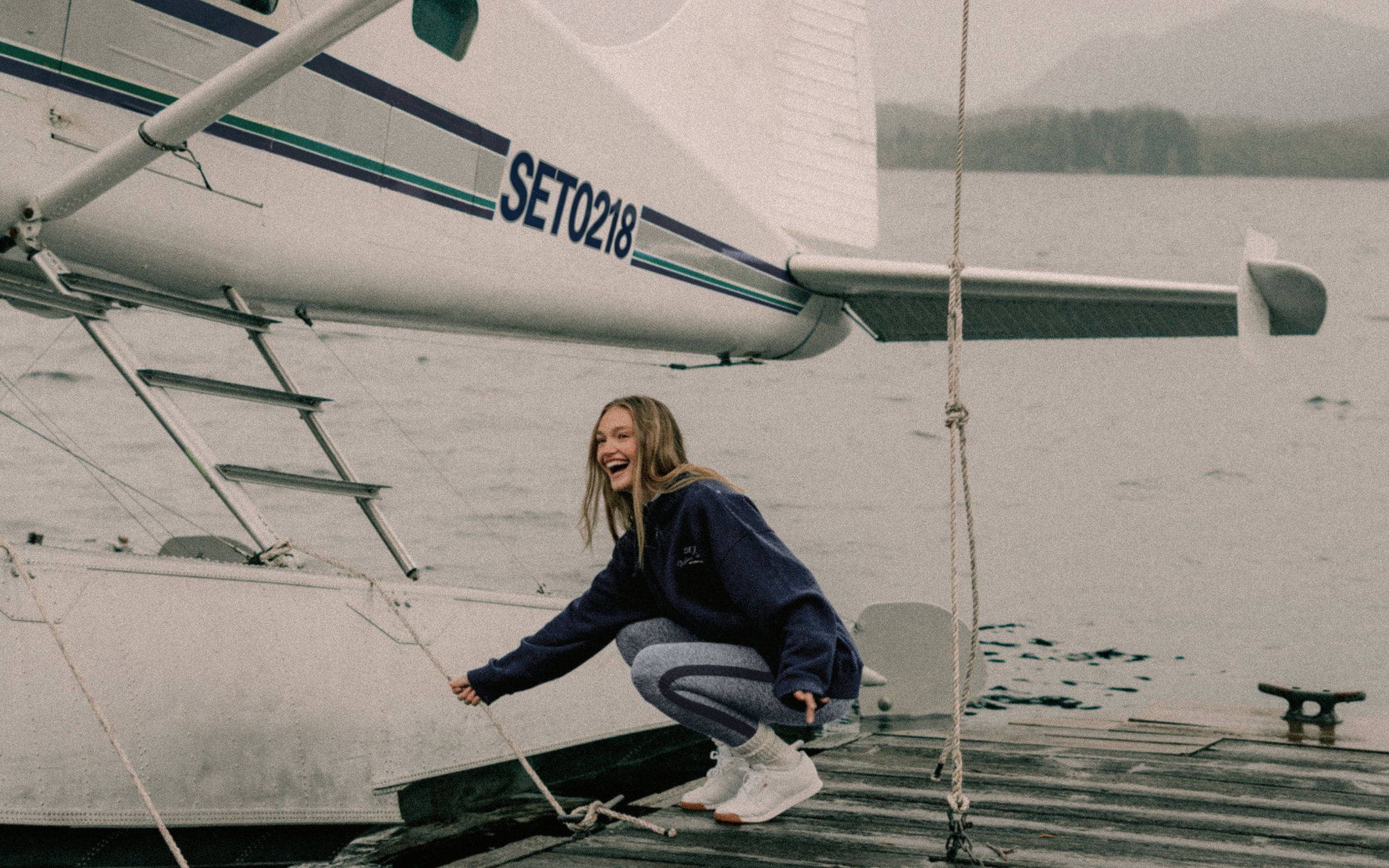 Person standing on a seaplane with water and trees in the background