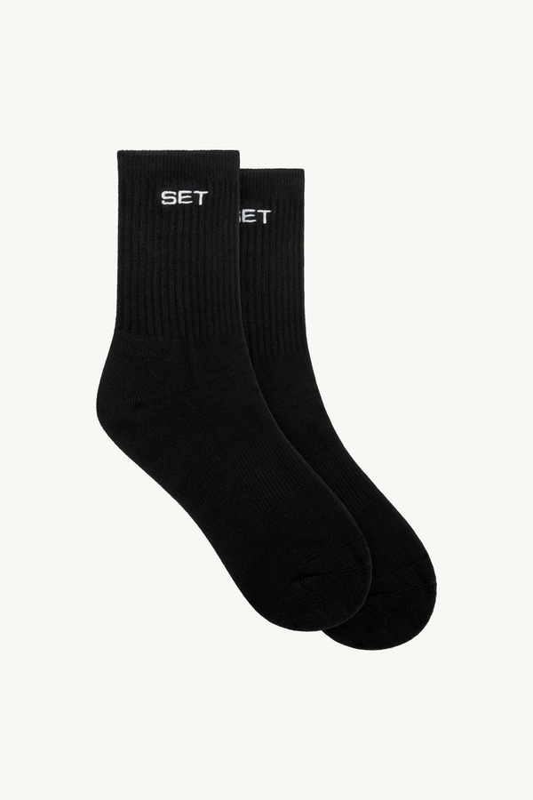 Pair of black socks with 'SET' logo on a beige background 