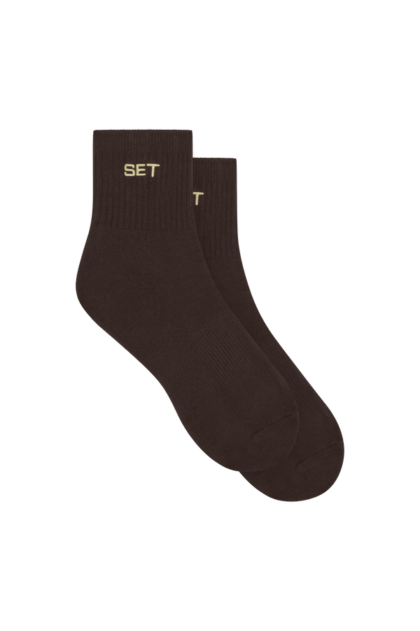 A pair of dark brown ankle socks with the word 'SET' embroidered in gold on the ribbed cuffs, displayed against a solid white background.