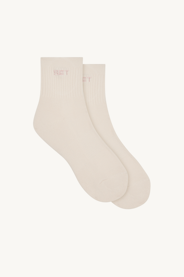Pair of beige socks with pink logo on a white background