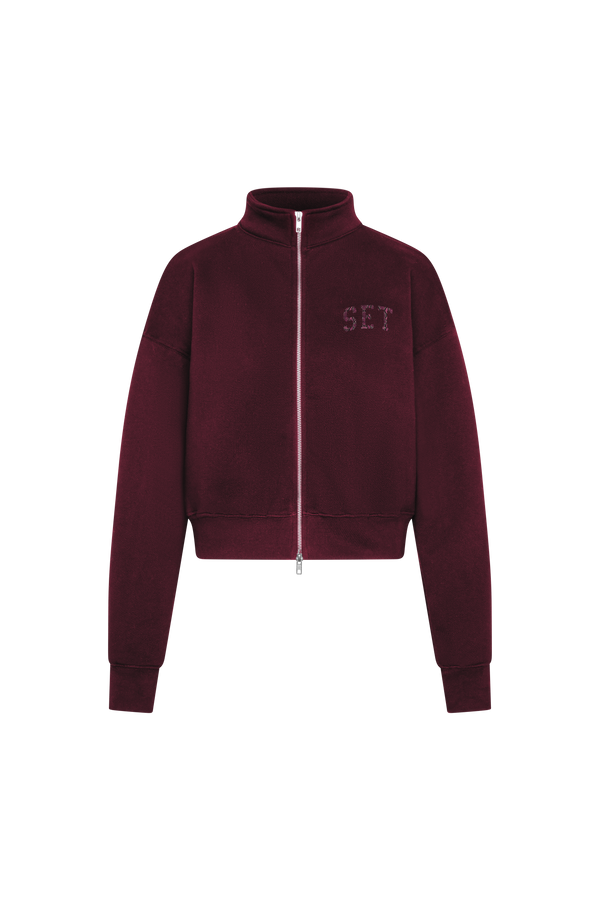 A cropped zip-up jacket in deep burgundy, featuring a stand-up collar, a front zipper, and the letters 'SET' embroidered in matching burgundy on the left chest, shown against a plain white background.