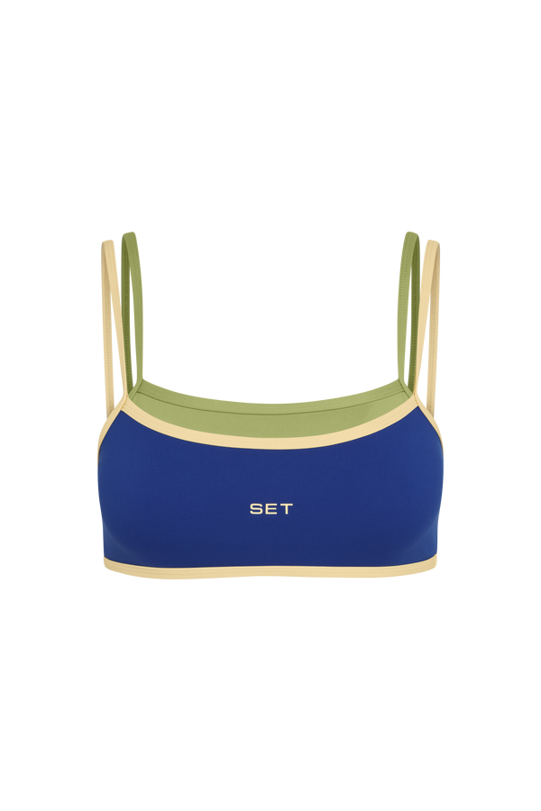 A women's sports bra by SET, featuring a royal blue main body with light beige trim, an olive green inner band, and matching olive green shoulder straps, shown against a plain white background.