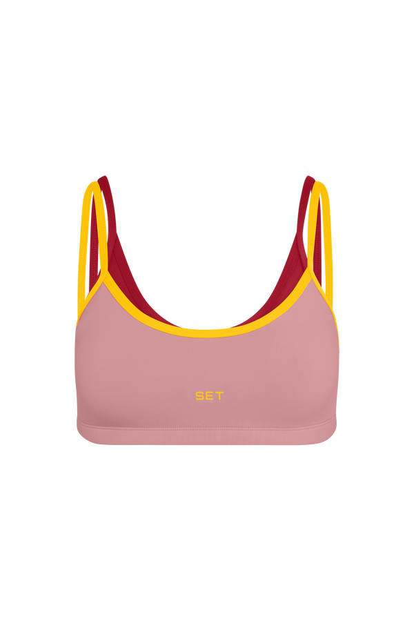 A pink sports bra with yellow trim and double straps, featuring a small yellow 'SET' logo on the front, displayed against a solid white background.