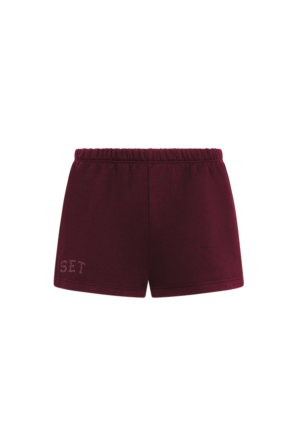 A pair of dark burgundy fleece shorts with an elastic waistband and a tonal embroidered 'SET' logo on the lower left leg, shown against a plain white background.