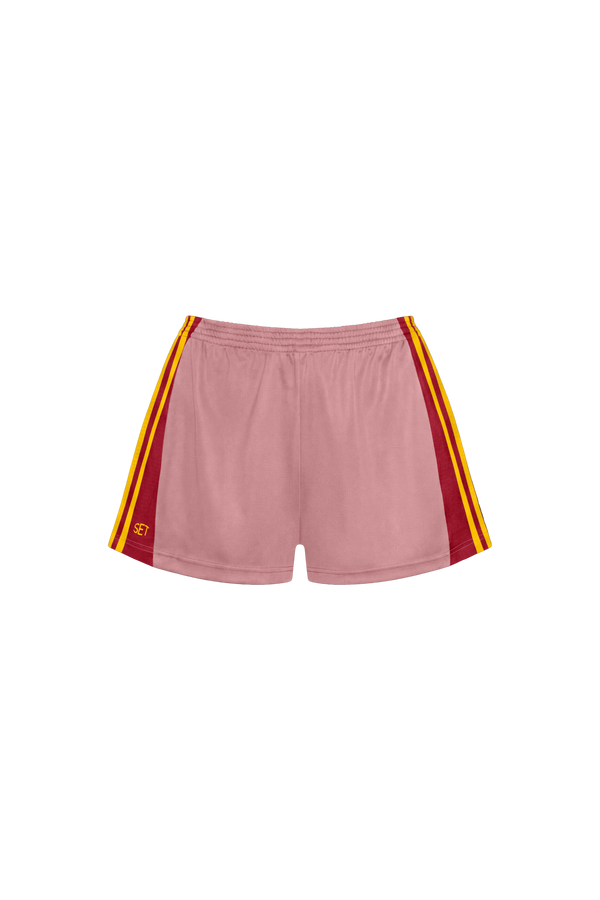 A pair of dusty pink athletic shorts with red and yellow side stripes, featuring a small yellow logo on the lower left leg, displayed against a solid white background.