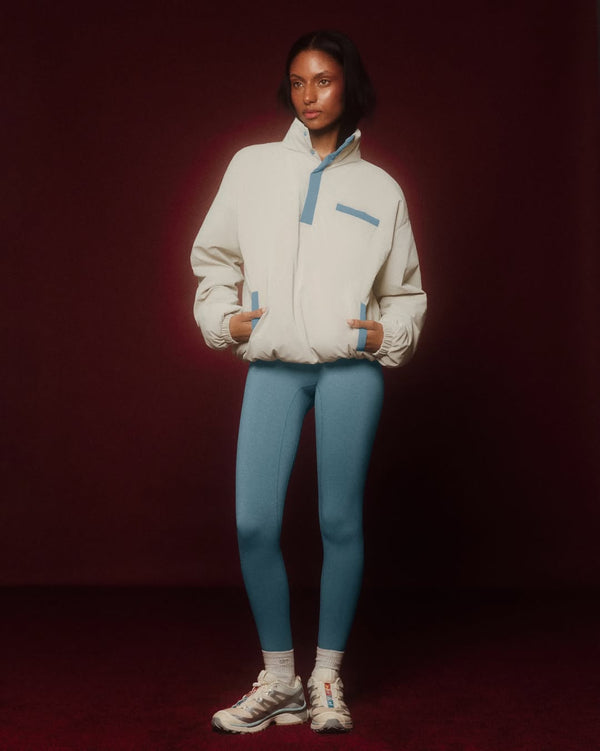 Person wearing a light gray jacket with blue accents and blue leggings on a dark red background