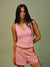 A woman modeling a pink athletic crop top and matching pink shorts with red and yellow side stripes, posed against a muted green studio background. <model-info>Jelene wears a size S and is 5’7”, 23” waist, 32AB bust.</model-info>