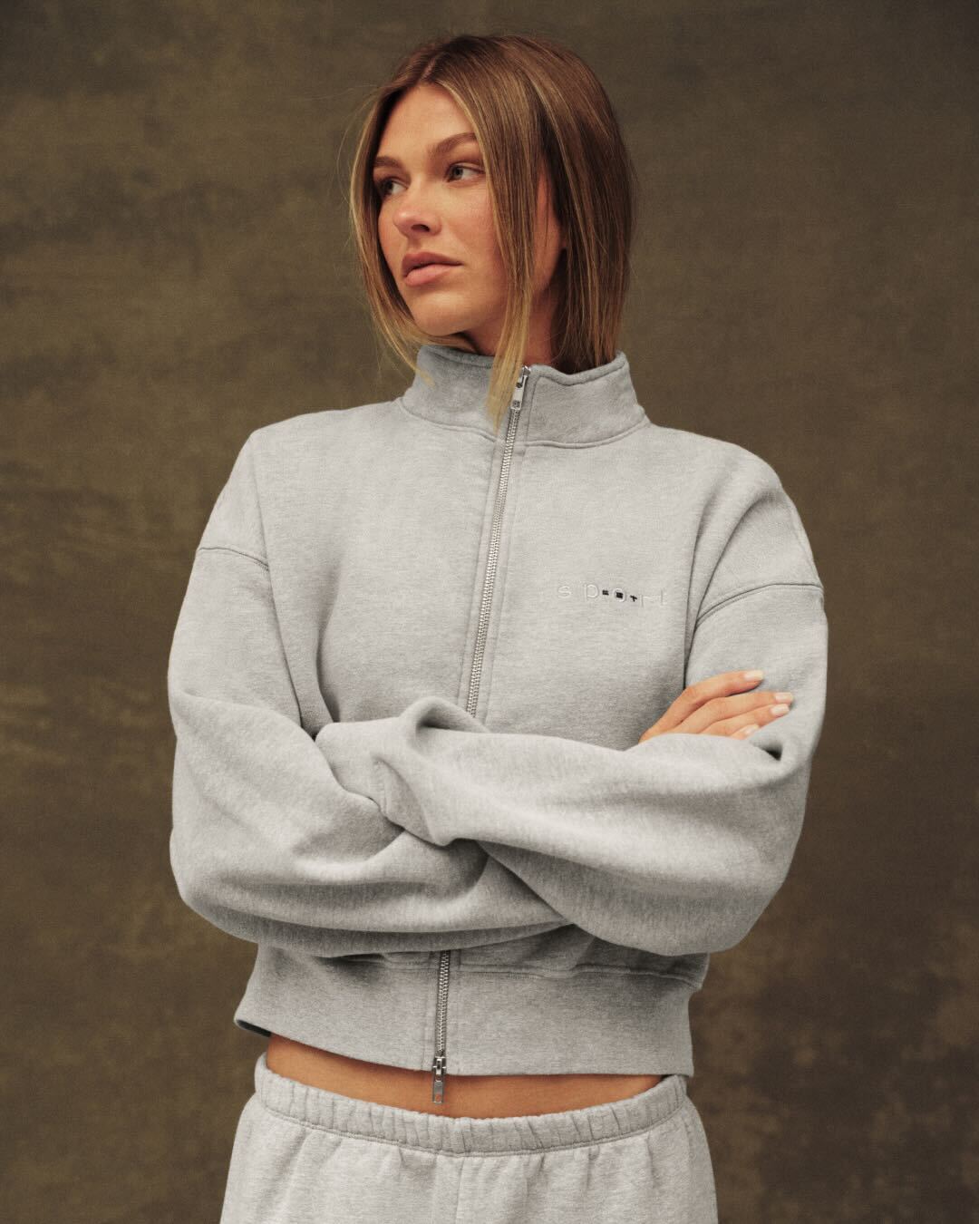 Woman wearing a gray tracksuit against a brown background