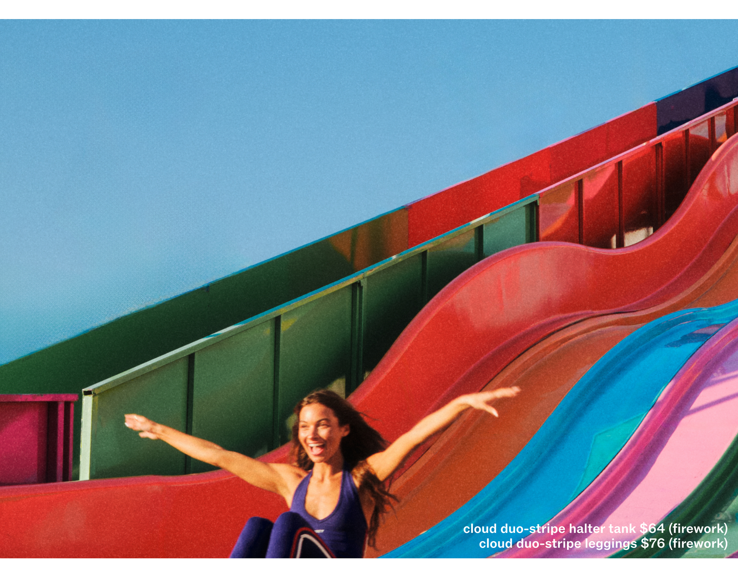 Woman sliding down a colorful slide with a clear blue sky above