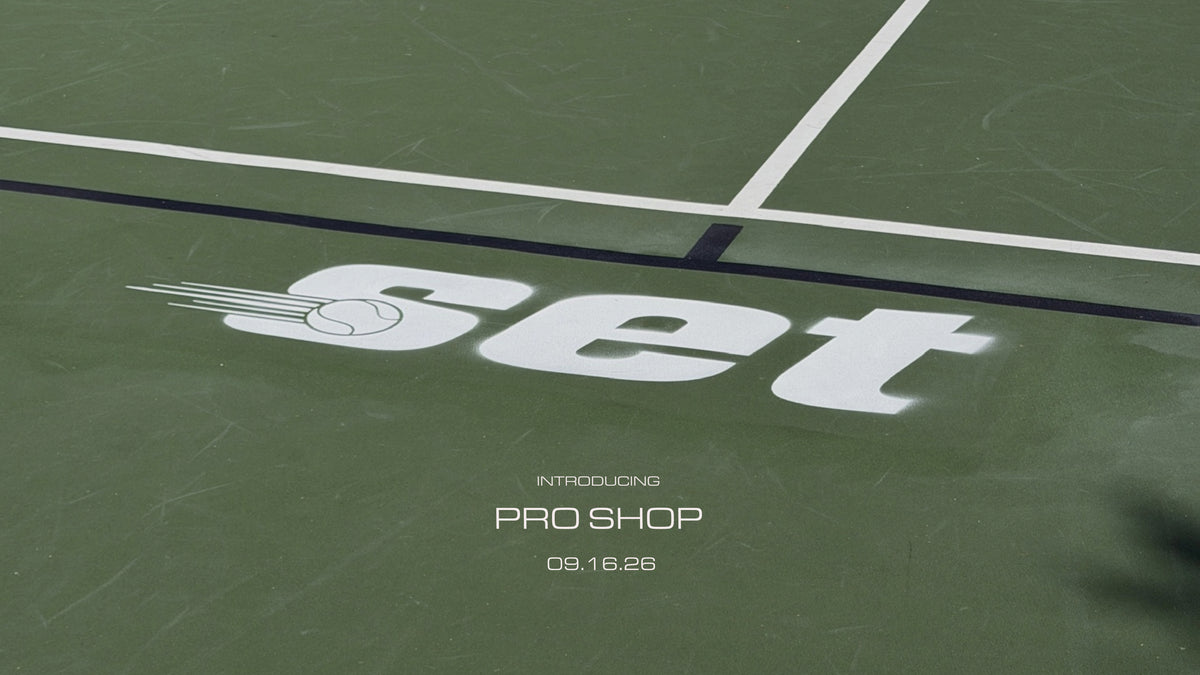A green tennis court surface with white boundary lines and the word 'set' in large white letters. Small centered text reads 'INTRODUCING PRO SHOP 09.