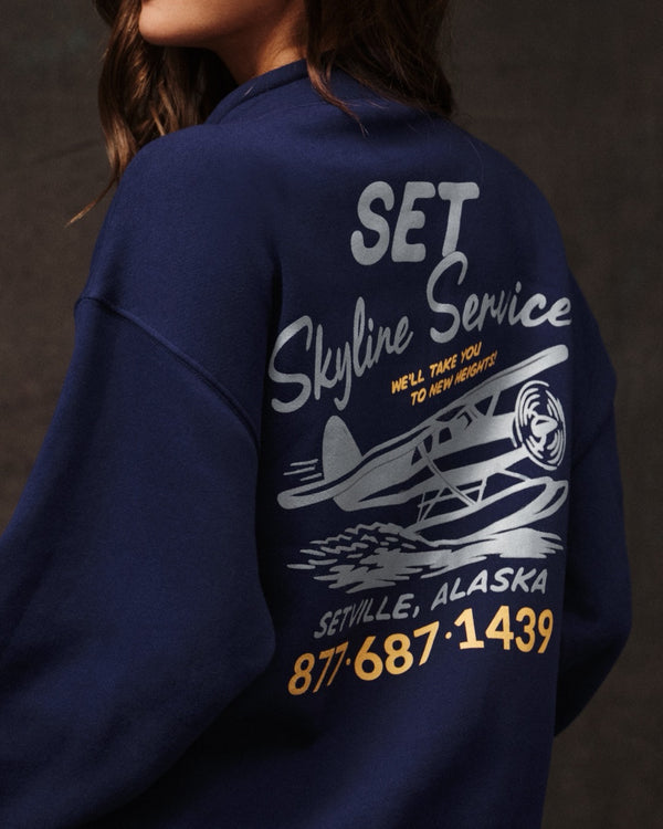 Navy blue sweatshirt with 'Set Skyline Service' text and airplane graphic on a dark background