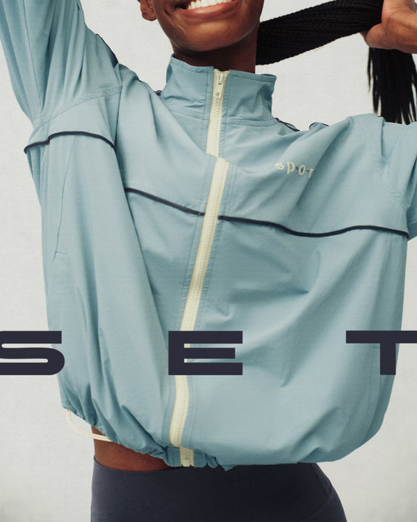 Person wearing a light blue jacket with a brand logo, standing against a plain background.