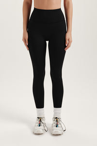 Person wearing black leggings and white sneakers on a light gray background 