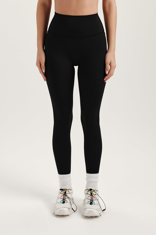 Person wearing black leggings and white sneakers on a light gray background 