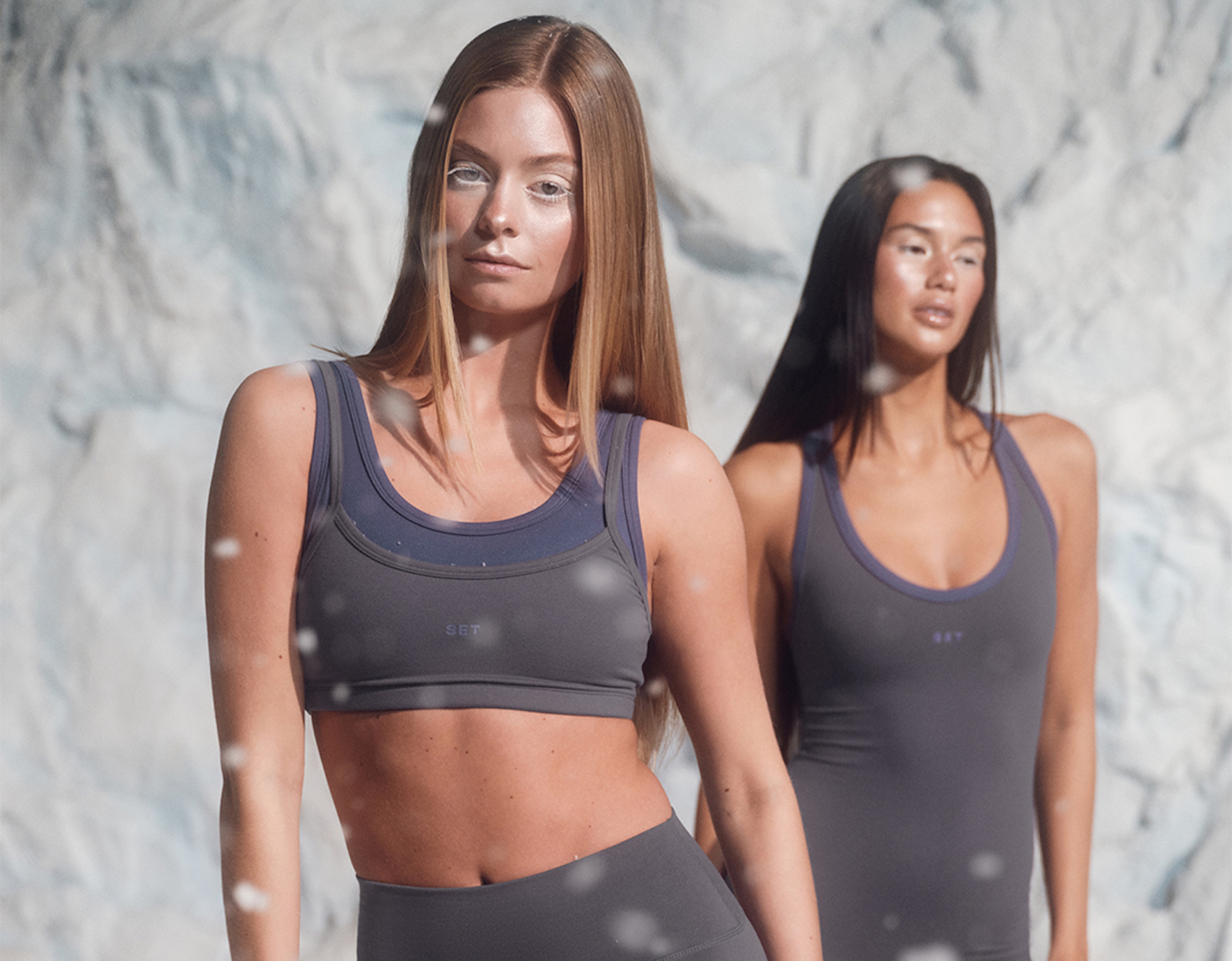 Two women wearing gray sports bras and leggings against a snowy background