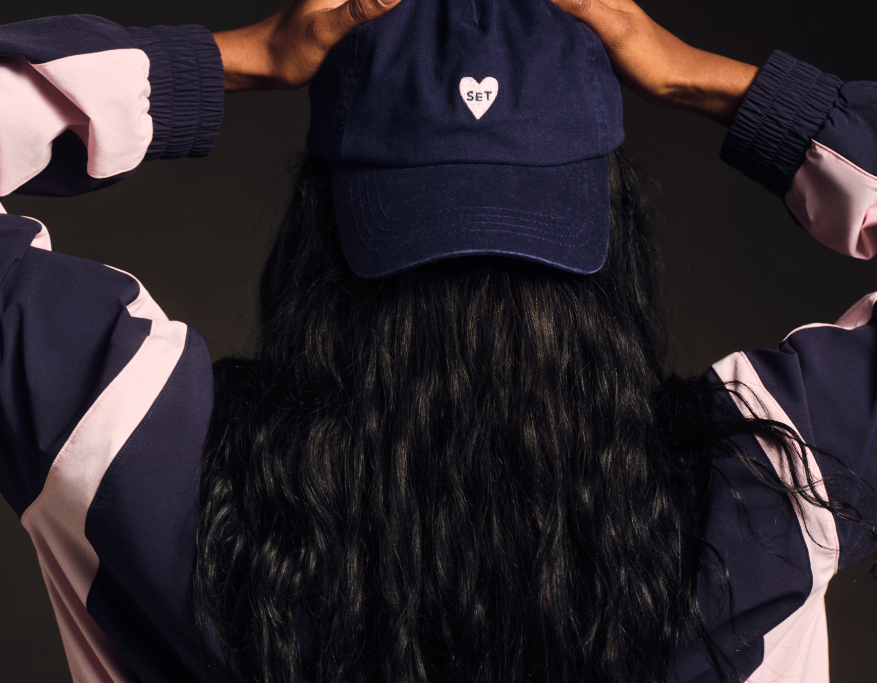 Person wearing a navy blue cap with a heart logo against a dark background