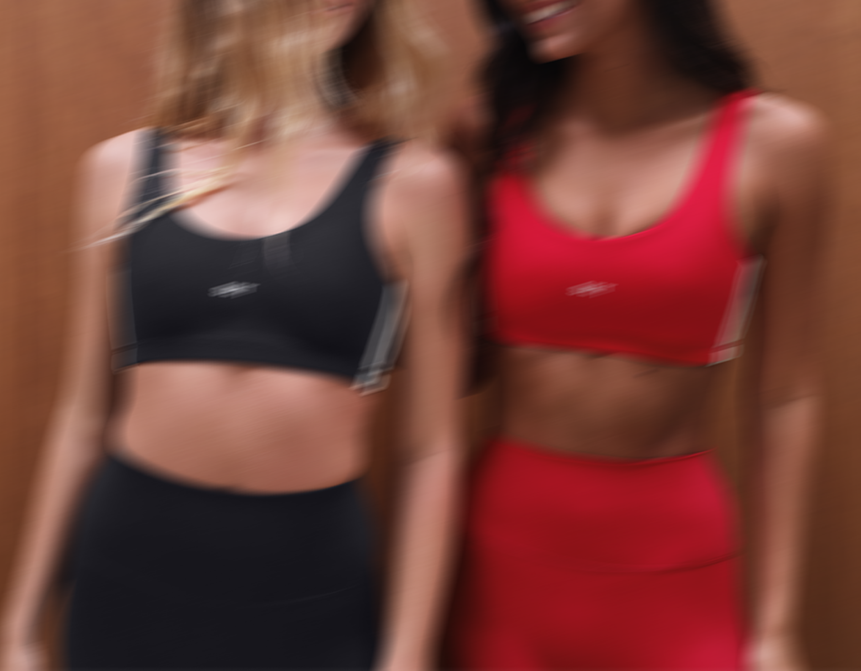 Two women wearing sports bras and leggings with a brand logo on a brown background