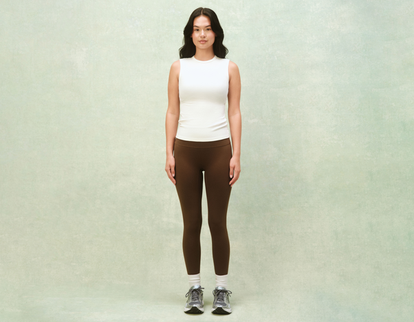 Girl wearing white tank and brown leggings in front of a light green background