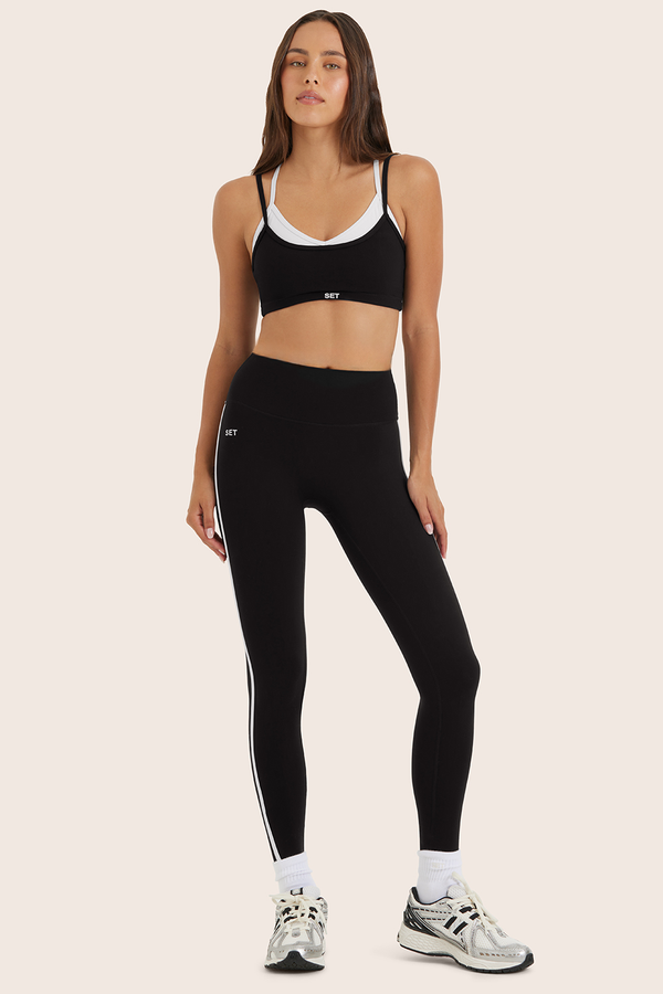 Woman wearing black athletic leggings and sports bra on a beige background