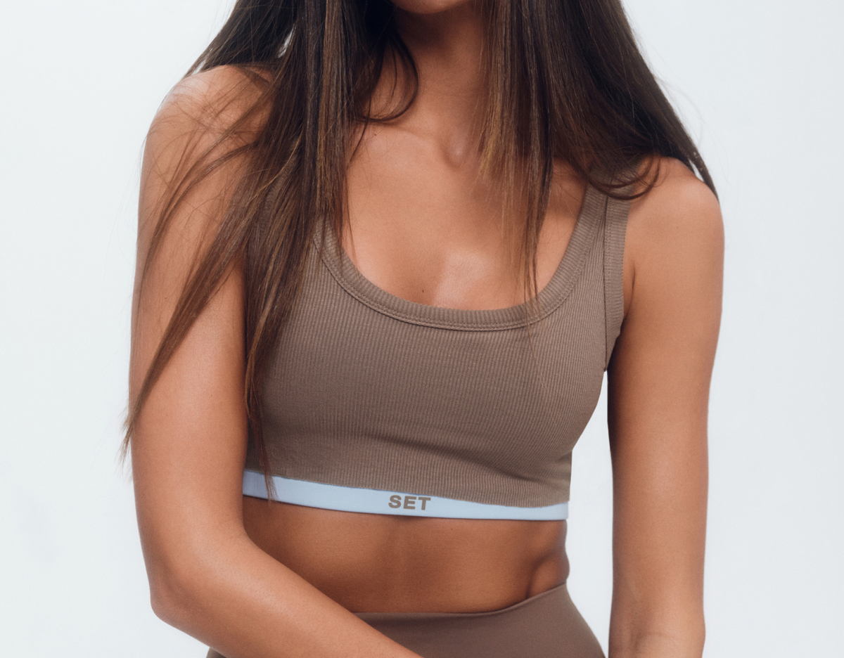 Woman wearing a brown sports bra with a white waistband on a light gray background